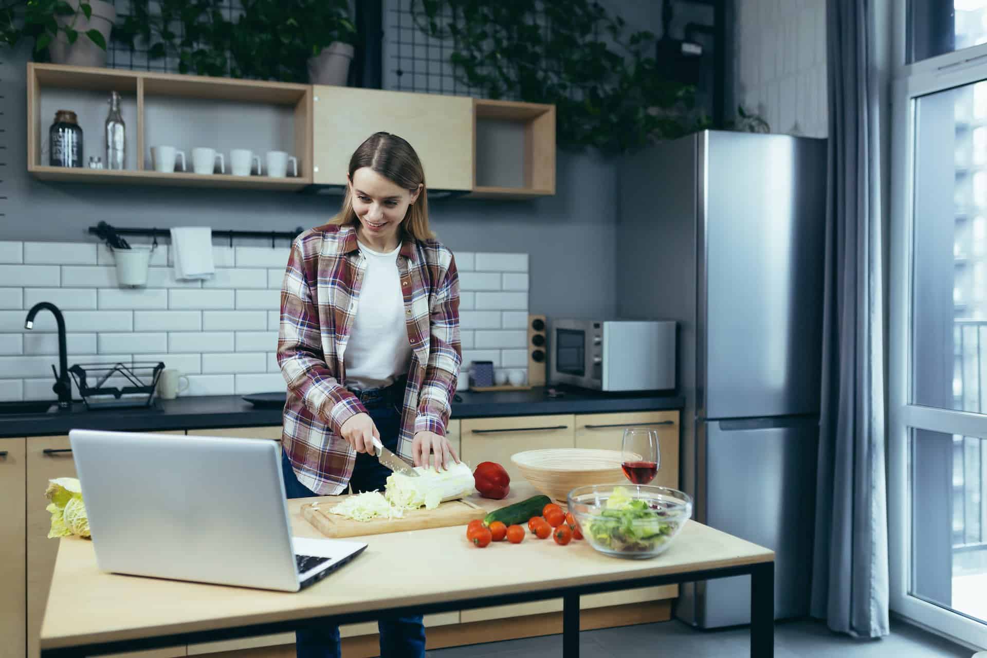 Young beautiful woman cooks, learns online cooking, blonde at home cuts vegetables